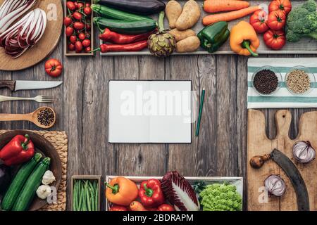 Fresh healthy vegetables, chopping boards and cooking utensils composing a frame on a vintage kitchen worktop, blank open cookbook at center Stock Photo