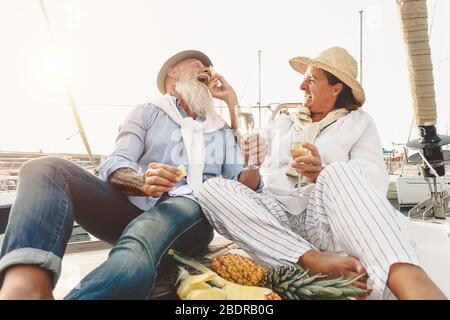 Senior couple drinking champagne eating pineapple on sailboat vacation - Happy mature people having fun celebrating wedding anniversary on boat trip Stock Photo