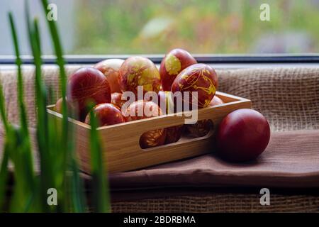 Easter eggs are coloured by ancient onion husk method with various natural patterns lying by window in sunshine on beige burlap next to the sprouted g Stock Photo