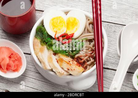 Asian noodle ramen soup with chicken, vegetables and eggs and herbal tea on wooden table Stock Photo