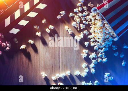 Popcorn and clapper on a wooden desktop, dramatic lighting, cinema and movies concept Stock Photo
