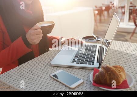Young woman having breakfast on a cafe terrace and working on her computer Stock Photo