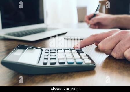 close-up shot of person using pocket calculator while taking notes on office desk Stock Photo