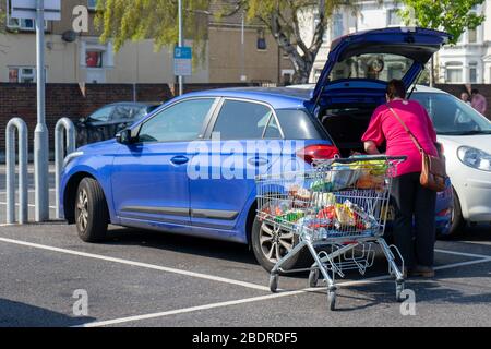 A middle aged woman unloading her shopping trolley full of shopping into the boot of her car or trunk of her car Stock Photo