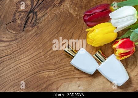 Two white perfume bottles and a bouquet of multi-colored tulips on a natural Board. Copy space