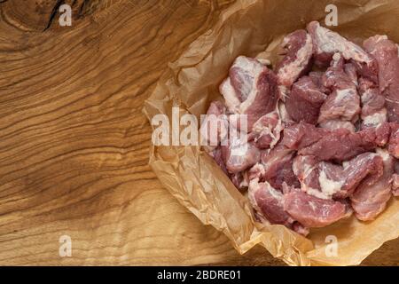 A piece of pork cut into pieces on paper lies on a wooden surface. Copy space Stock Photo