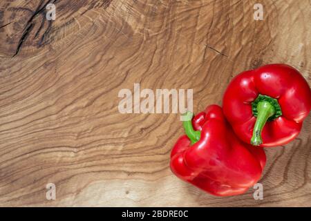 Two large, fleshy red peppers lie on the corner of a wooden table. Copy space Stock Photo