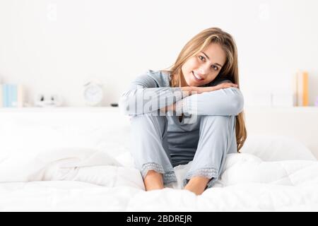 Happy young woman waking up and sitting on bed, she is smiling at camera Stock Photo