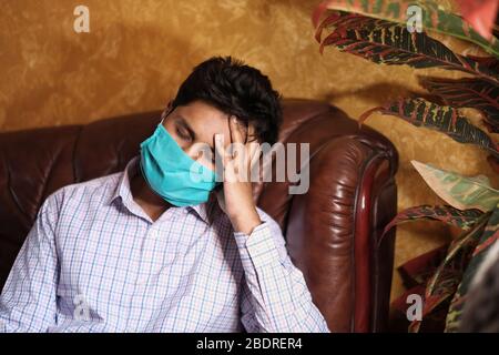 Sick young man with headache wearing protecting mask sitting on sofa  Stock Photo