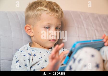 Caucasian child boy using digital tablet while lying on bed at home Stock Photo