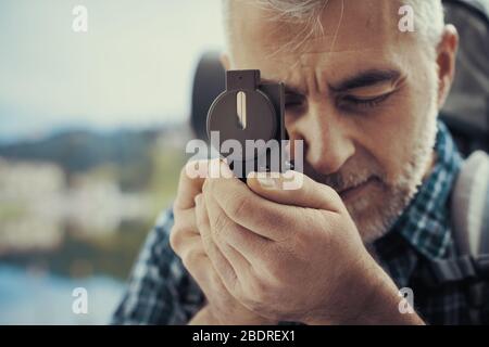 Hiker trekking on the mountains and exploring nature, he is using a hiking compass and searching directions Stock Photo