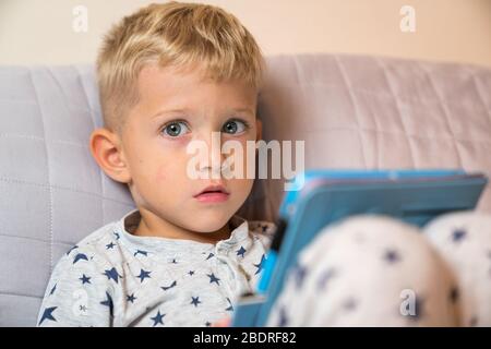 Caucasian kid boy using digital tablet while lying on bed at home Stock Photo