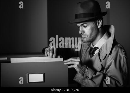 Vintage undercover criminal spy stealing files in a filing cabinet late at night, security and data theft concept Stock Photo