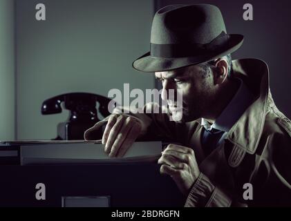 Vintage undercover criminal spy stealing files in a filing cabinet late at night, security and data theft concept Stock Photo