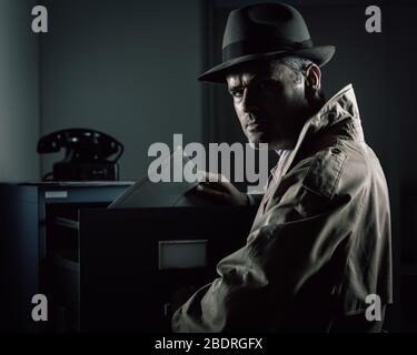 Vintage undercover spy stealing files in a filing cabinet late at night, security, data theft and crime concept Stock Photo