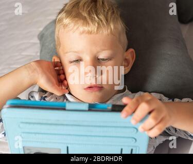Caucasian kid boy using digital tablet while lying on bed at home Stock Photo