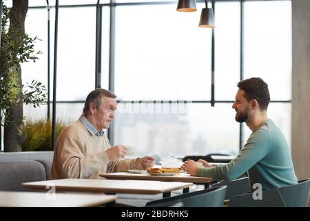 Two men sitting at the table having breakfast and talking to each other in the restaurant Stock Photo