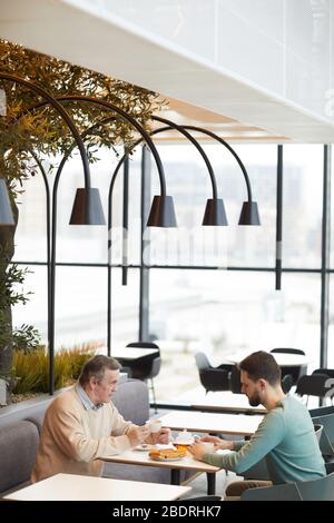 Mature father talking to his son while they sitting at the table and drinking tea in cafe Stock Photo