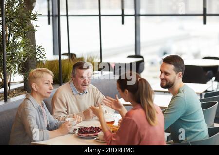 Family of four sitting at the table having breakfast together and talking to each other in cafe Stock Photo