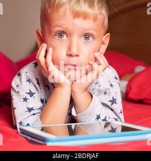 Caucasian child boy using digital tablet while lying on bed at home Stock Photo