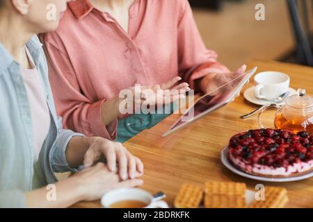 Close-up of two women using digital tablet while sitting at the table and drinking tea with fruit cake Stock Photo