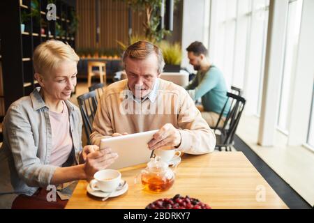 Mature couple using digital tablet while drinking tea at the table in the restaurant Stock Photo