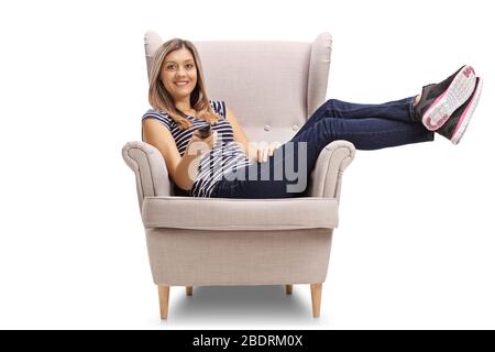 Young woman sitting in a cosy armchair and holding a remote control isolated on white background Stock Photo