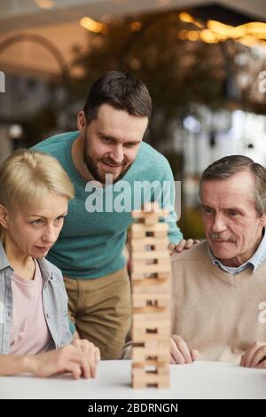 Group of people concentrating on the game they looking at heap of wooden details and playing in Jenga together Stock Photo