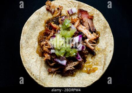Carnitas tacos with red onion and raw salsa verde. Mexican slow cooked pork dish isolated on black plate Stock Photo