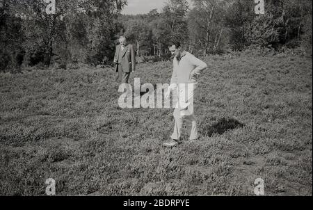 1960s, historical, 'in the rough', not a good place to be on a golf course, a golfer and a gentleman in a three-piece suit, look on the ground for the players missing golf ball, England, UK. A golfer has only a certain number of minutes (was 5, now only 3 minutes) to search and find his golf ball, otherwise he has to go back and hit another shot from the spot where the original ball was last played. Stock Photo