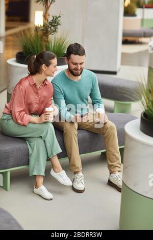 Young couple drinking coffee and using mobile phone while sitting on sofa in the mall Stock Photo
