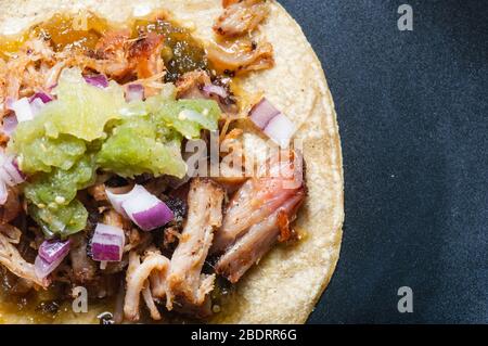 Carnitas tacos with red onion and raw salsa verde. Mexican slow cooked pork dish isolated on black plate Stock Photo