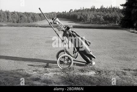 1960s, historical, Outside on a golf course, sat on a tee, a leather golf bag with clubs on a wire-wheeled golf trolley of the era. Stock Photo