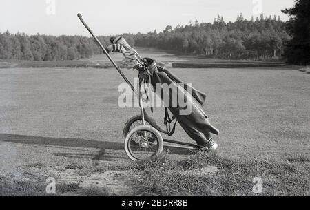 1960s, historical, Outside on a golf course, sat on a tee, a leather golf bag with clubs on a wire-wheeled golf trolley of the era. Stock Photo