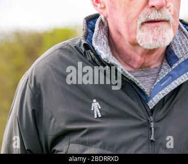 Senior man with grey beard wearing Prostate Cancer UK charity badge pin pinned to jacket to raise awareness of common health condition, United Kingdom Stock Photo