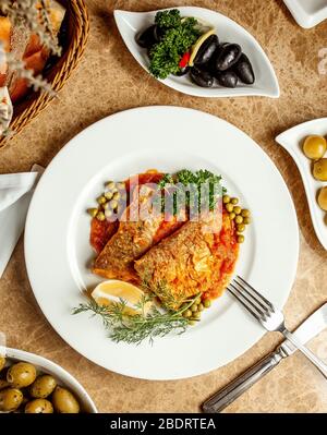 fish fillets in tomato sauce served with peas lemon and herbs Stock Photo