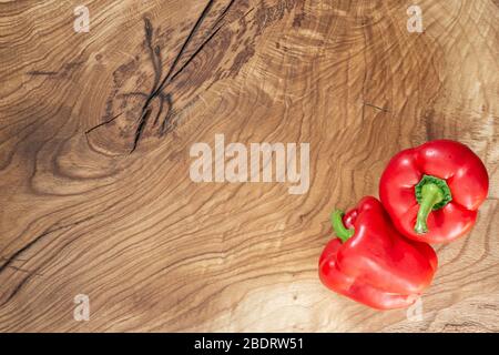 Two large fleshy red peppers lie on the corner of a natural wooden table. Copy space Stock Photo