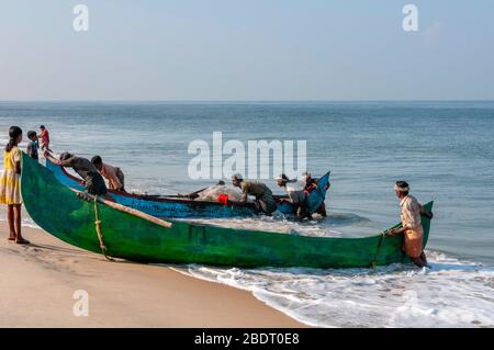 Fishermen hauling their traditional wooden boat from the sea on Marari Beach following an early morning fishing trip. Kerala, India Stock Photo