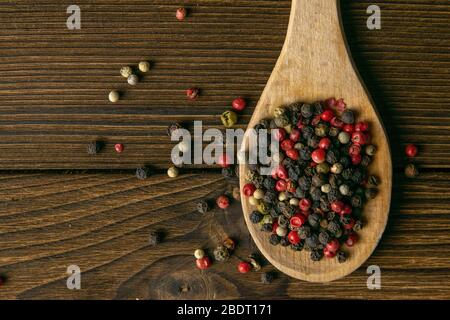 Multi-colored pepper on a wooden spoon and sprinkled side by side on a wooden table. Top views Stock Photo