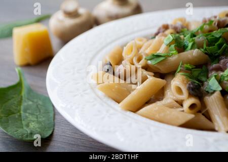 Vegan creamy mushroom garlic pasta with red onions garnished with basil in a white plate with its ingredients in the background Stock Photo