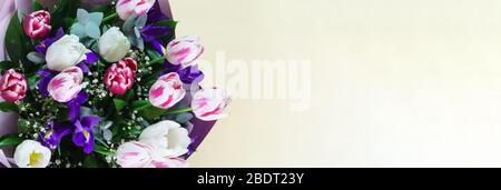 A bright spring bouquet with tulips and irises in a gift box lies on the yellow table. Copy space Stock Photo