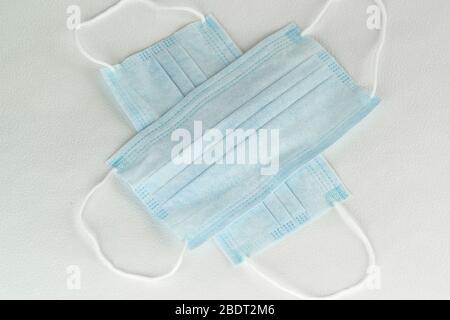 Two simple disposable medical masks made of non-woven fabric lie on a white table. The view from the top Stock Photo