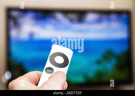 Man presses a button on the modern grey steel remote controll on the background of the TV turned off. A man controls a TV Stock Photo