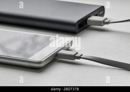 The smartphone is charging from external powerbank with cable. White background, closeup, selective focus Stock Photo