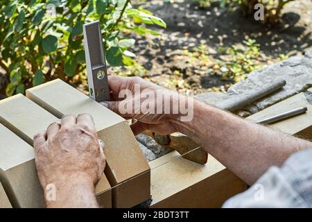 Bricklayer levelling bricks on the new fence from facing bricks using building level. Stock Photo