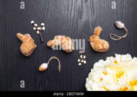 chocolate willow branches and cute bunnies with eggs, narcissus flowers on black wooden background, happy Easter greeting card, spring festive season. Stock Photo