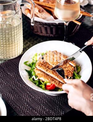 woman cutting sesame crusted chicken served with salad