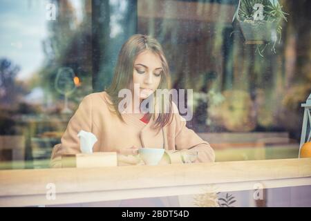 Portrait young gorgeous woman female drinking tea and thoughtfully looking out of the coffee shop window while enjoying her leisure time alon, nice bu Stock Photo