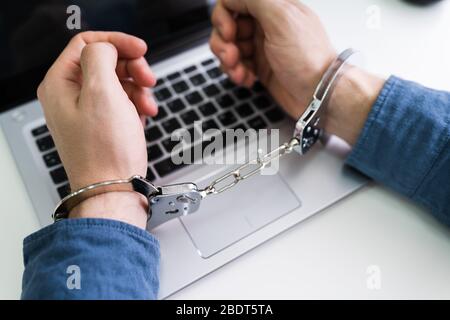 Close-up Of Person's Hand With Handcuff Using Laptop Stock Photo