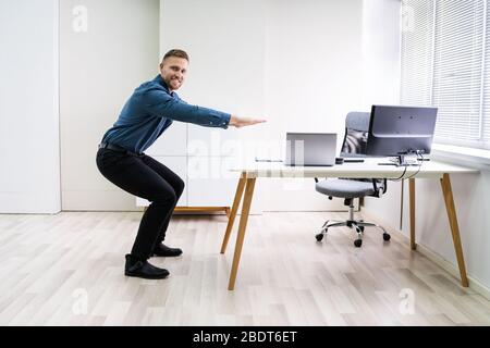 Smiling Young Businessman Doing Sit-ups At Workplace Stock Photo